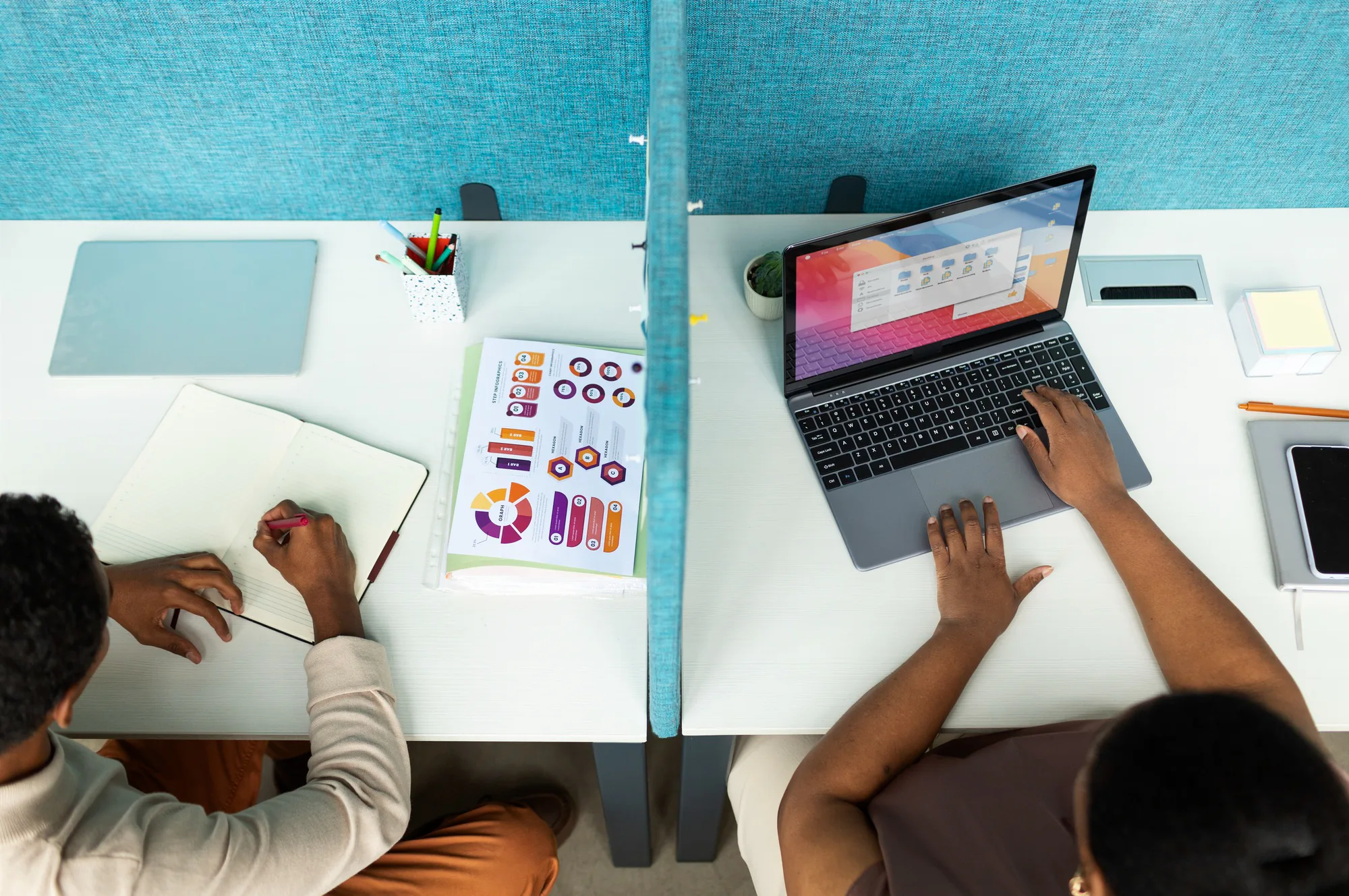Two collaborators developing ideas with a laptop, notebook and planning diagrams